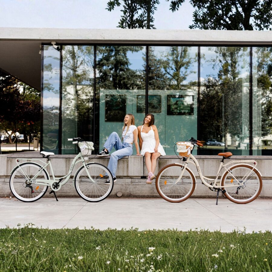 Femei zâmbitoare lângă biciclete în fața clădirii moderne.
