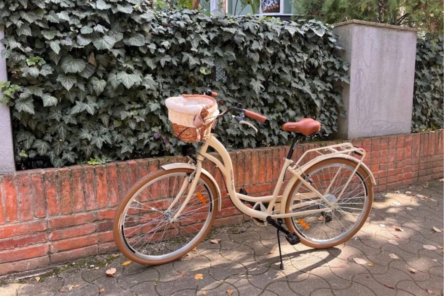 Bicicletă beige cu coș împletit lângă zid.