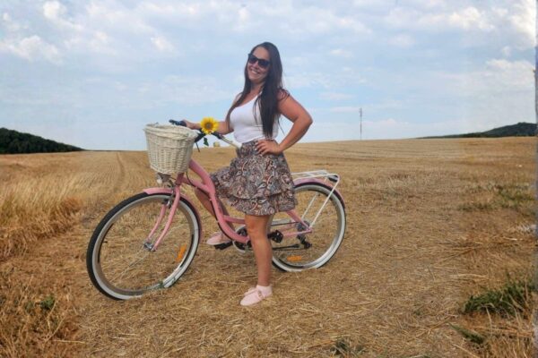 Femeie cu bicicleta roz în lan de grâu.