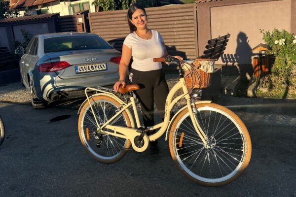 Femeie lângă bicicletă albă, zâmbind în soare.