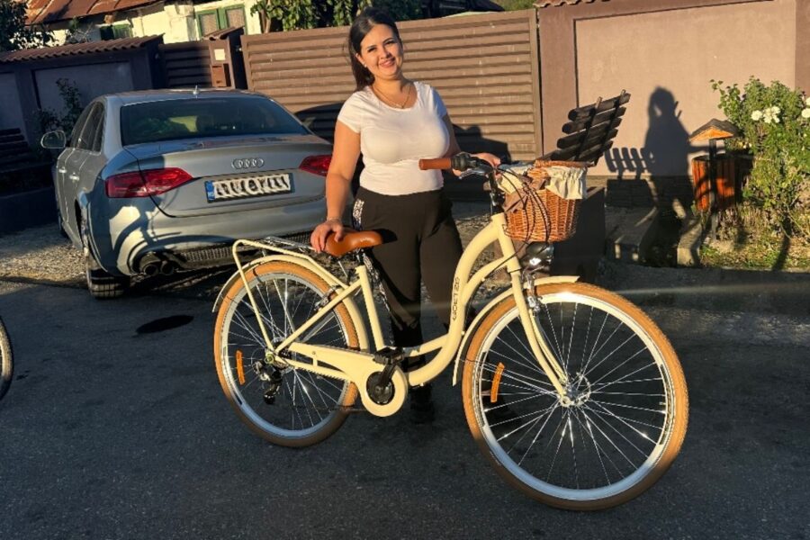 Femeie lângă bicicletă albă, zâmbind în soare.