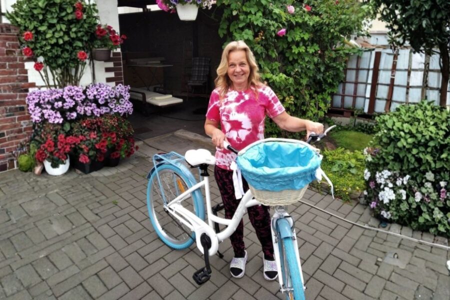 Femeie zâmbitoare lângă bicicletă alb-albastră, grădină cu flori.