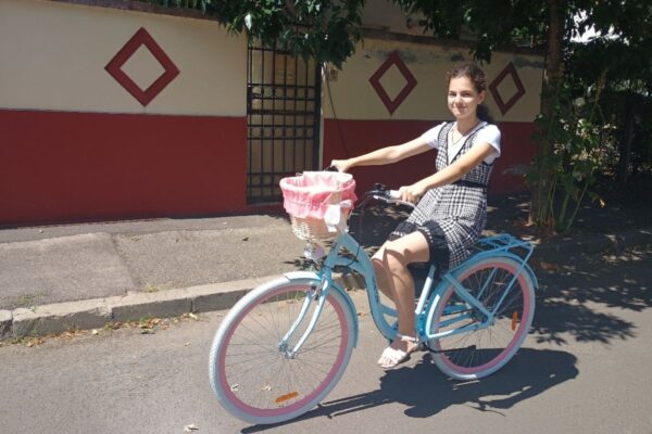Fată pe bicicletă albastră, zâmbind pe stradă.